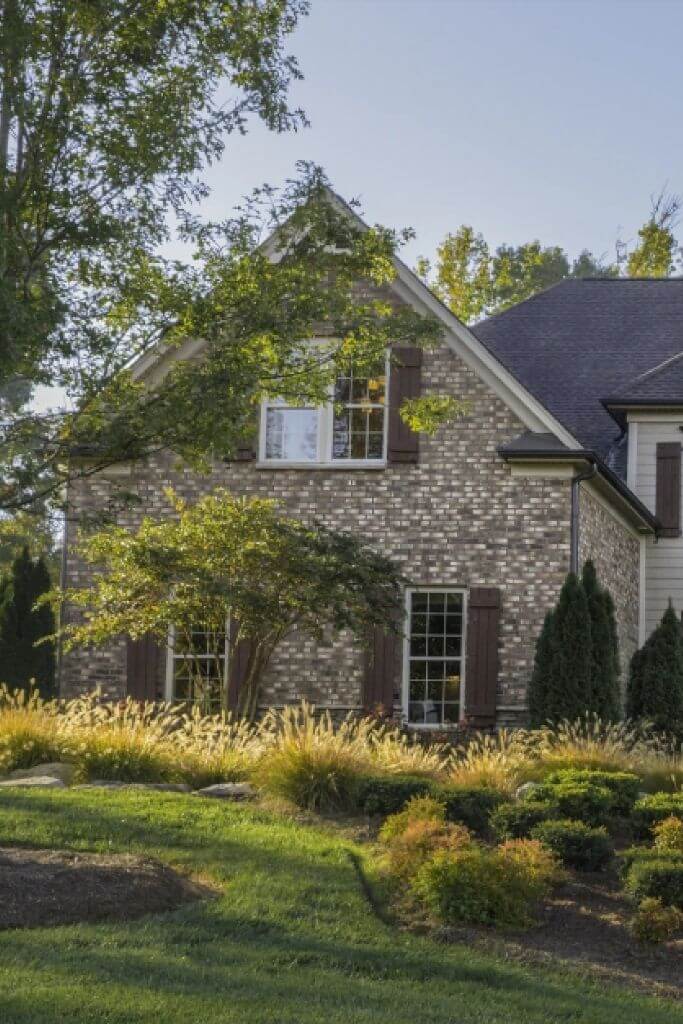 A home exterior with grey and brown brick and green landscaping.