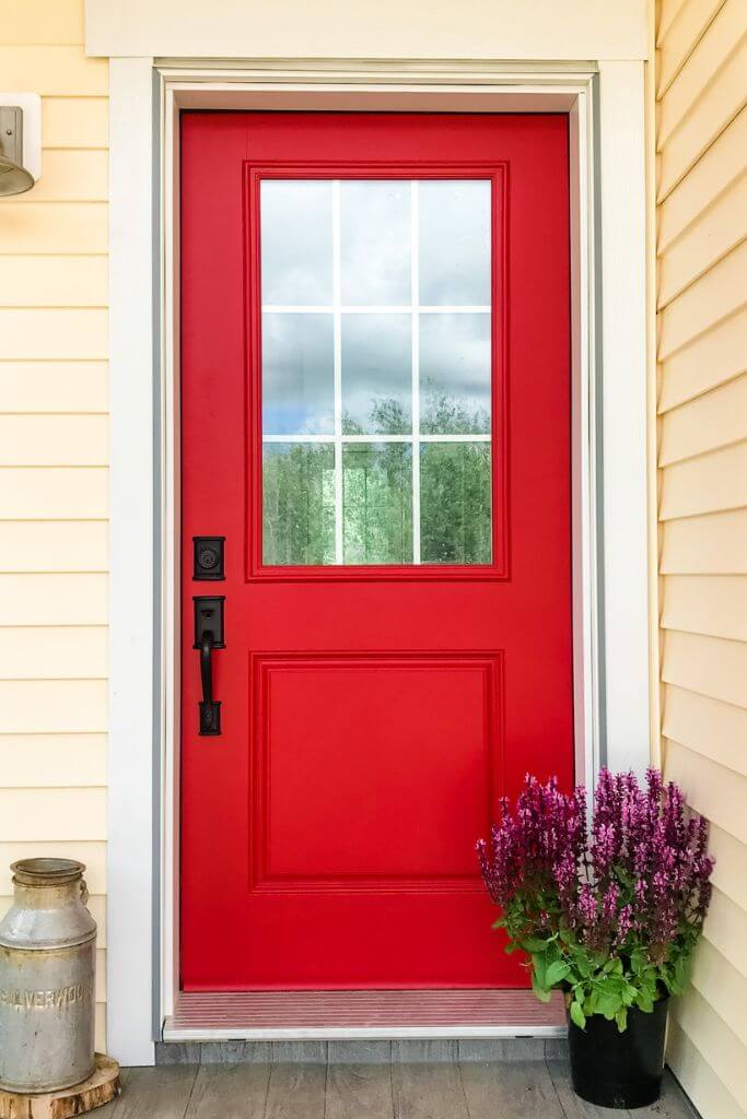 A home with yellow horizontal vinyl siding and a red door.