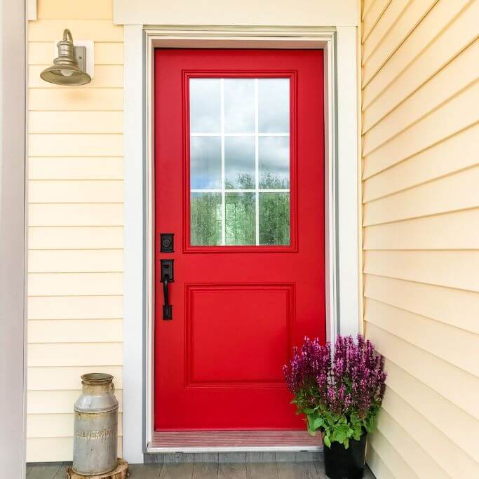 A home exterior with yellow horizontal vinyl siding and a red door.