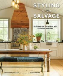 Book cover of Styling with Salvage featuring a photo of a white kitchen with a wooden range hood and a large rustic table.