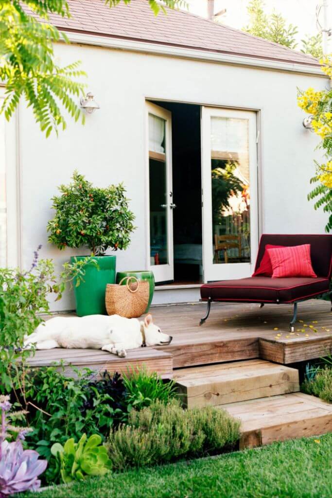 A wooden deck attached to a white home with a white dog sleeping on it.