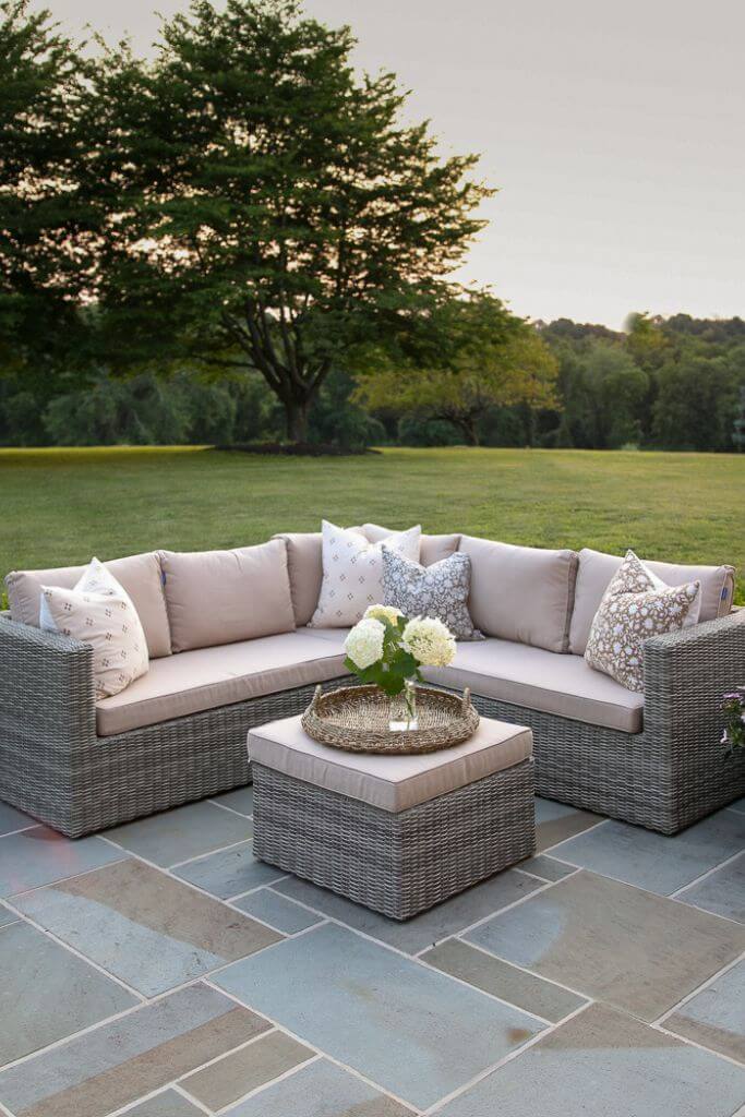 A stone patio with neutral coloured outdoor furniture surrounded by grass.