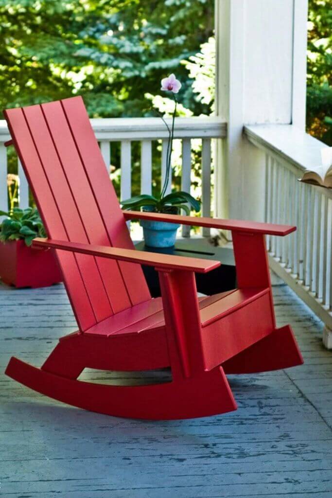 A red adirondack rocking chair on a white porch.