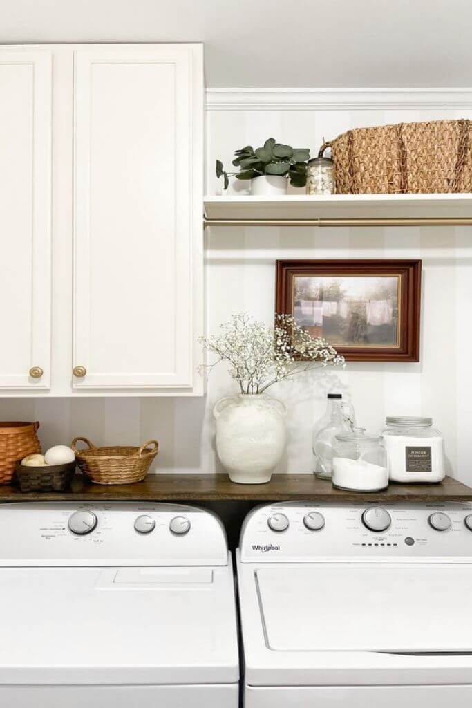 A laundry room with white cupboards, striped wallpaper and vintage accents.