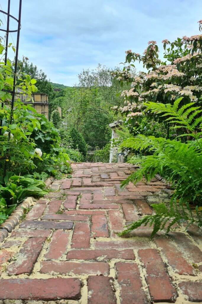 A red brick pathway lined with greenery and flowers.