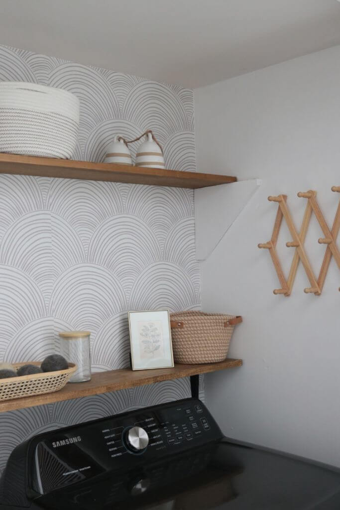 A laundry room with wooden shelves and a neutral coloured curve-patterned wallpaper.