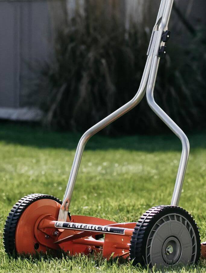 A red push lawnmower sitting on grass.