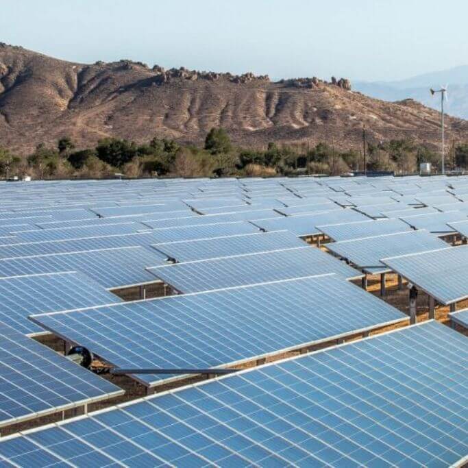 A large solar farm with mountains in the background.