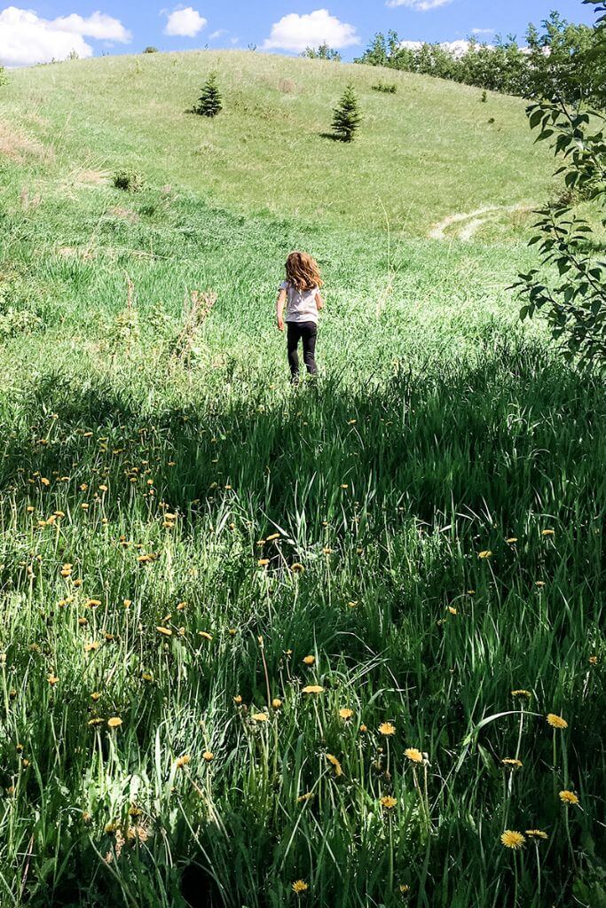 A little girl running up a green hill toward a blue sky.