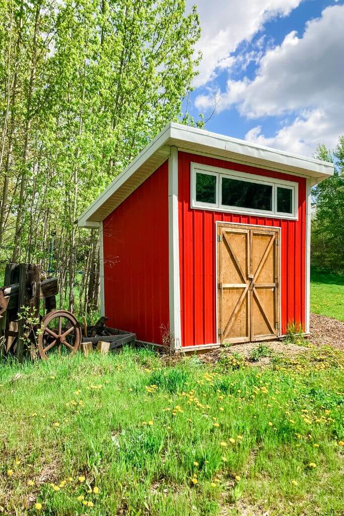 A bright red garden shed with a wooden door beside a piece of antique arm equipment.