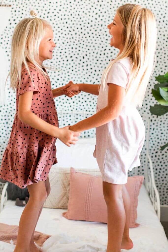 Two little girls holding hands and laughing with polka dot wallpaper in the background.