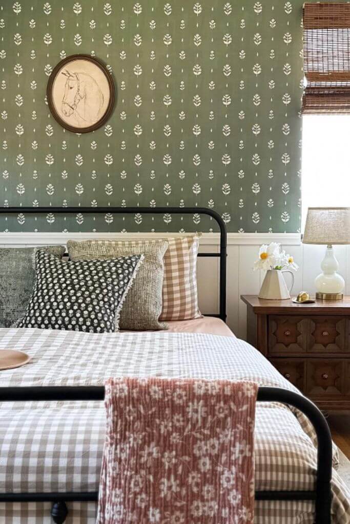 A bedroom with green floral wallpaper, a black metal bed and a drawing of a horse hanging on the wall.