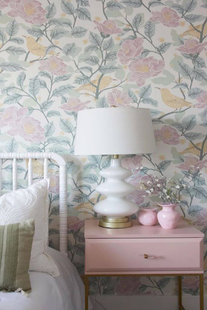 Floral wallpaper behind a white bed frame and pink nightstand.