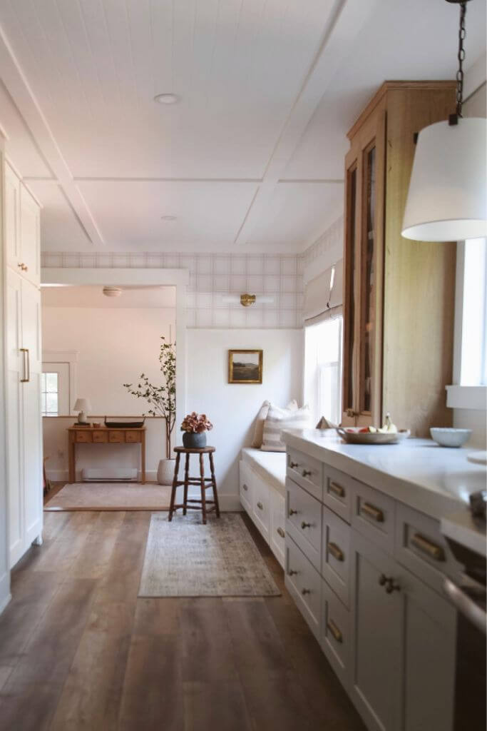 A kitchen with white cabinets and panelling and pink plaid wallpaper.