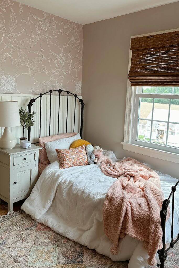 A kids's room decorated with pink floral wallpaper, a black metal bed frame and feminine accessories.