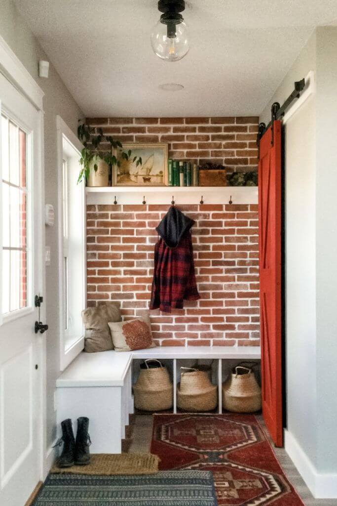 A home's entryway with red brick walls, a white bench and layered rugs.