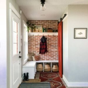 A front entrance with a reclaimed brick wall, a white bench, a red closet door and two vintage layered rugs.