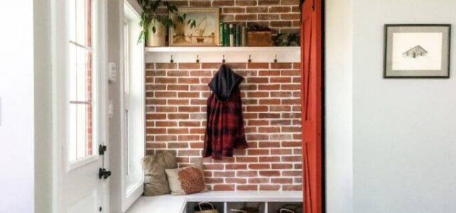 A front entrance with a reclaimed brick wall, a white bench, a red closet door and two vintage layered rugs.