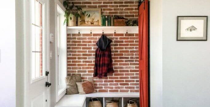 A front entrance with a reclaimed brick wall, a white bench, a red closet door and two vintage layered rugs.