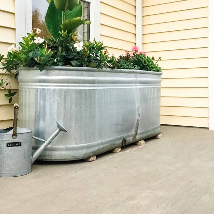 A metal flowerbed up against a yellow house with a grey deck.