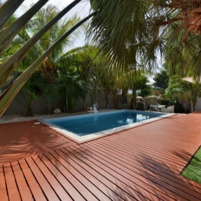 A dark wood-looking deck next to an in-ground backyard swimming pool.