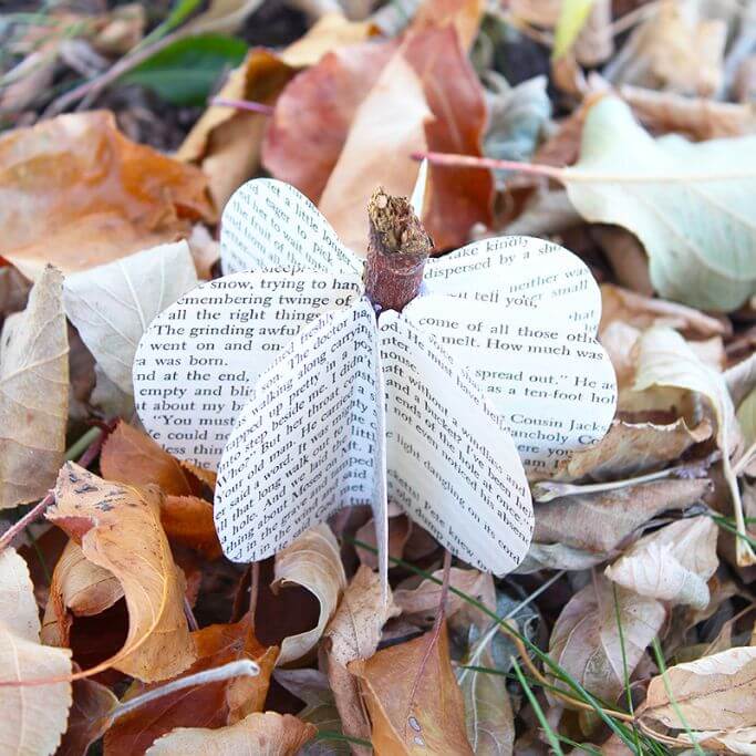 A paper pumpkin made from book pages sitting on a bed of dried leaves.