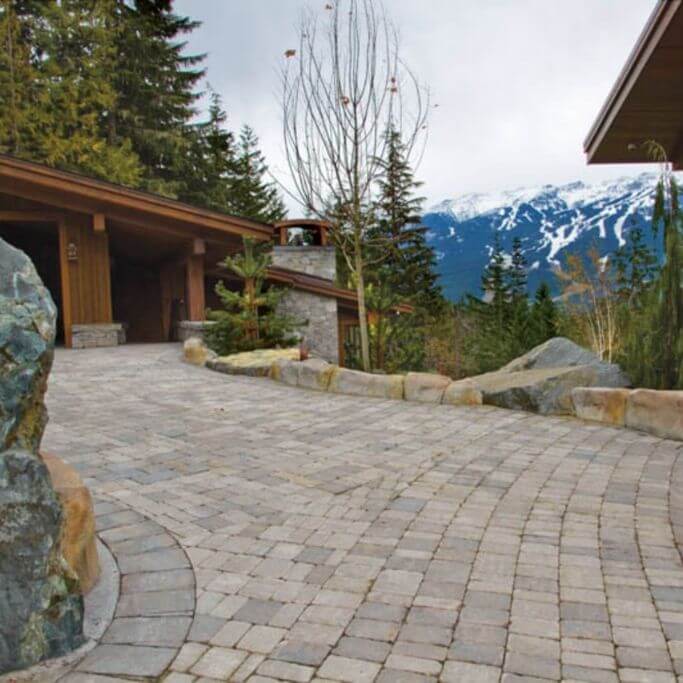 A concrete paver patio outside a dark brown home with mountains in the background.