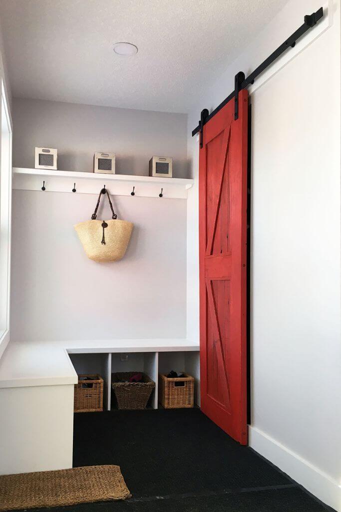 A small mudroom with a red barn door and a white built-in bench.