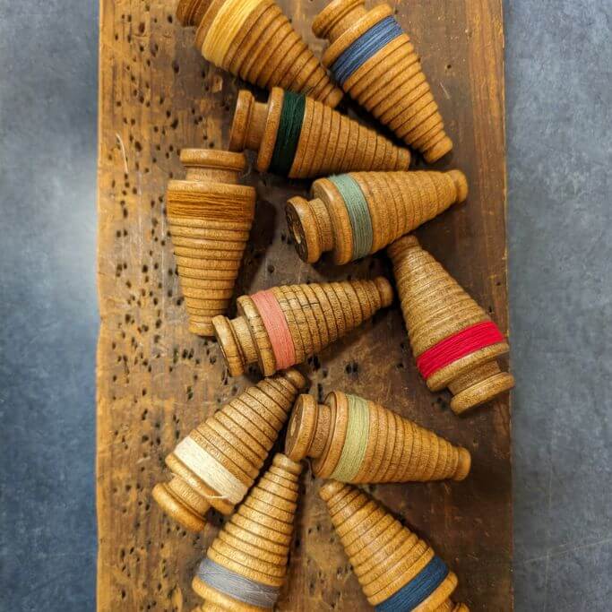 Wooden sewing bobbins shape like Christmas trees laying on a wooden table.