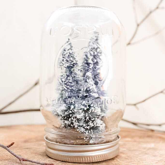 A handmade mason jar snow globe sitting on a tree slice.