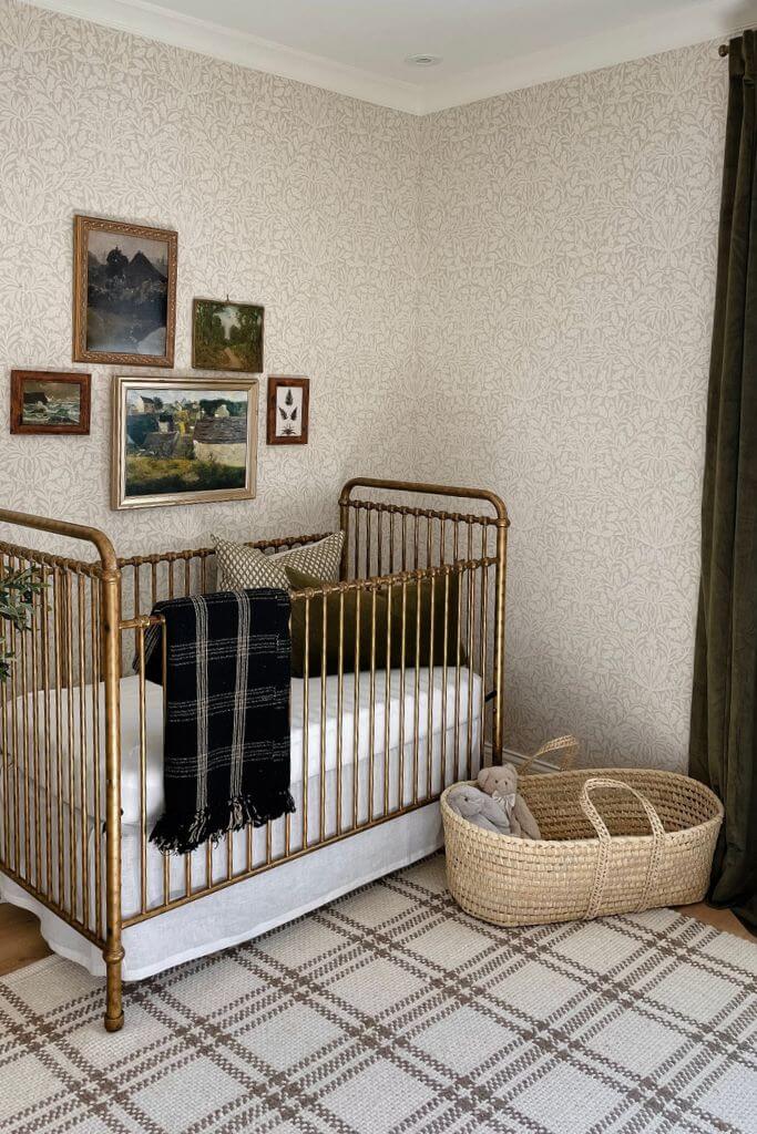 A nursery with vintage landscape art on the wall above a brass crib and next to a dark green curtain.