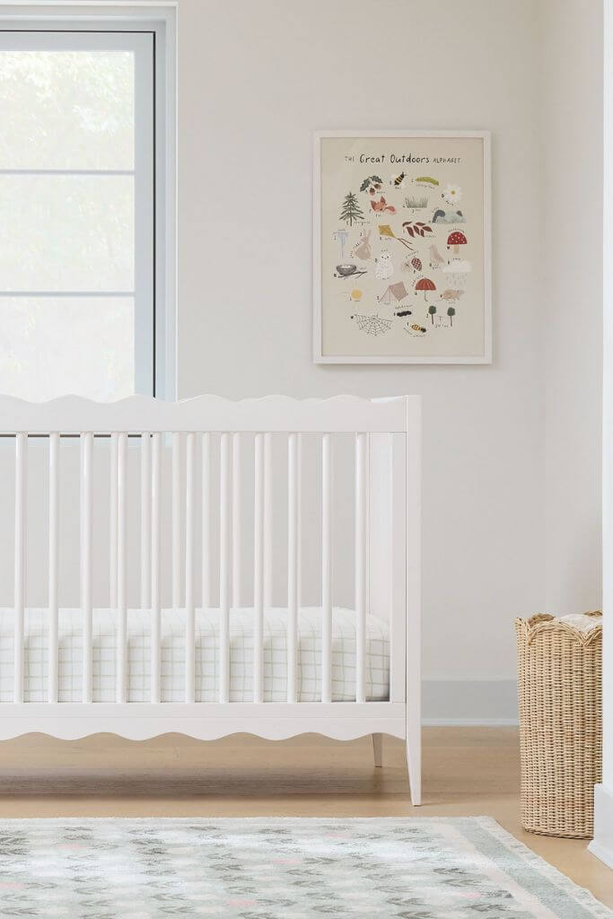 White wooden crib in a light-coloured nursery with a nature-themed poster on the wall.