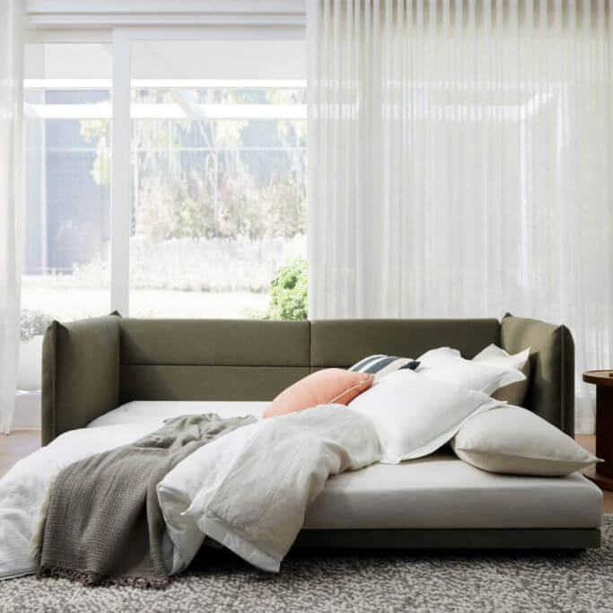 A dark green sleeper sofa puled out in a brightly lit living space.