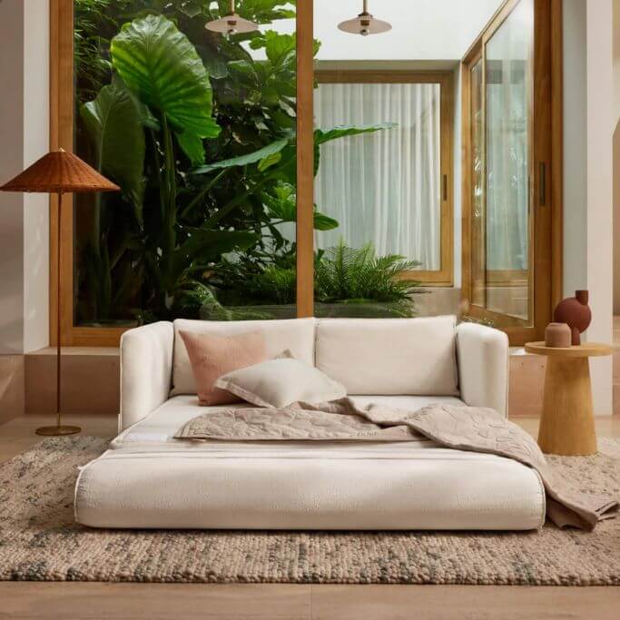 A white sleeper sofa pulled out in a living space with large wood-framed windows.