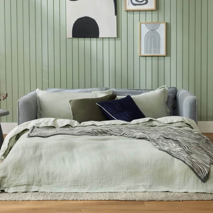 A grey sleeper sofa pulled out in a green living space.