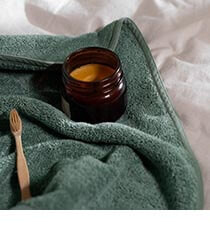 A brown glass jar and toothbrush on a green towel. Click to visit the Homebird website.
