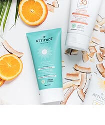 A blue bottle of sunscreen and a white bottle of sunscrenn on a white background surrounded with orange slices and coconut shavings. Click to visit the Attitude website.