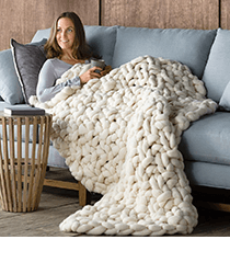 A woman sitting wrapped in a heavy knit blanket.