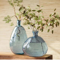 Two blue glass vases with greenery inside.