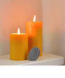 Two orange candles sitting on a white shelf. Click to visit the Bluecorn Beeswax website.