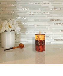 A red and yellow candle sitting next to a small wooden spoon and white flowers in a pot. Click to visit the Welljourn website.