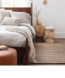 Plant Fibre Rug via The Citizenry A sand-coloured woven rug on a bedroom floor.