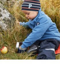 A toddler sitting outside eating from a lunch box.