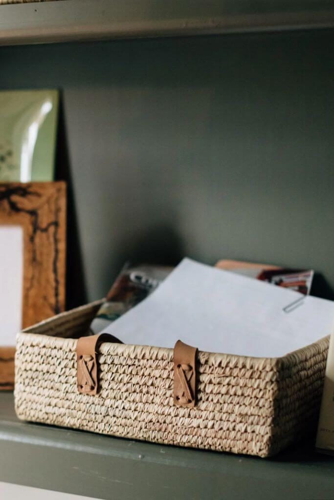 A woven storage basket in an office filled with loose paper.