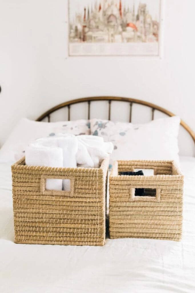 Two woven storage baskets on a bed filled with rolled up towels.